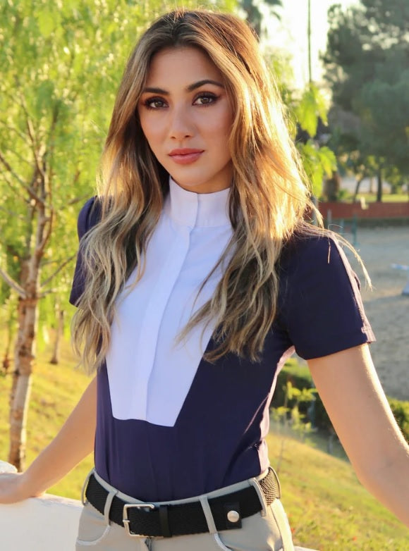 Woman wearing a navy and white equestrian outfit with a blurred outdoor background