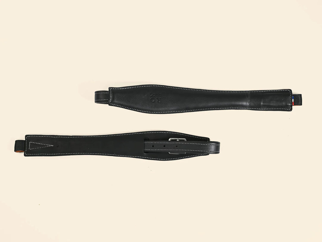 Two black leather girth straps on a beige background